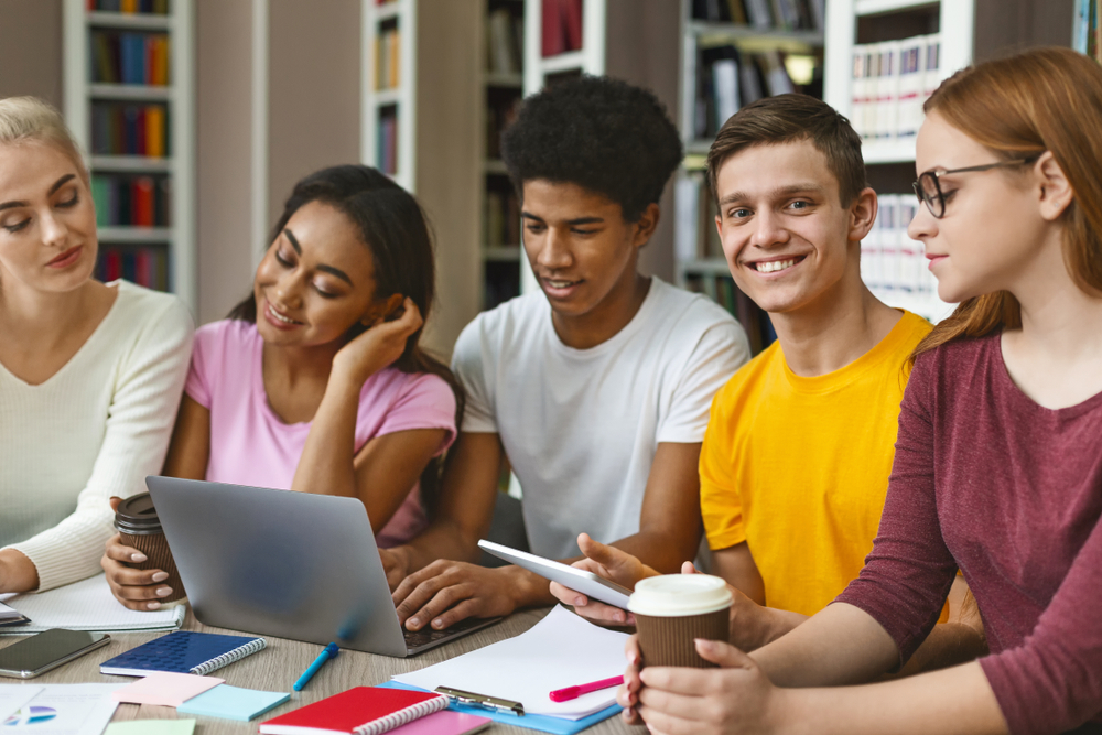 International students using tablet and laptop while studying, library interior