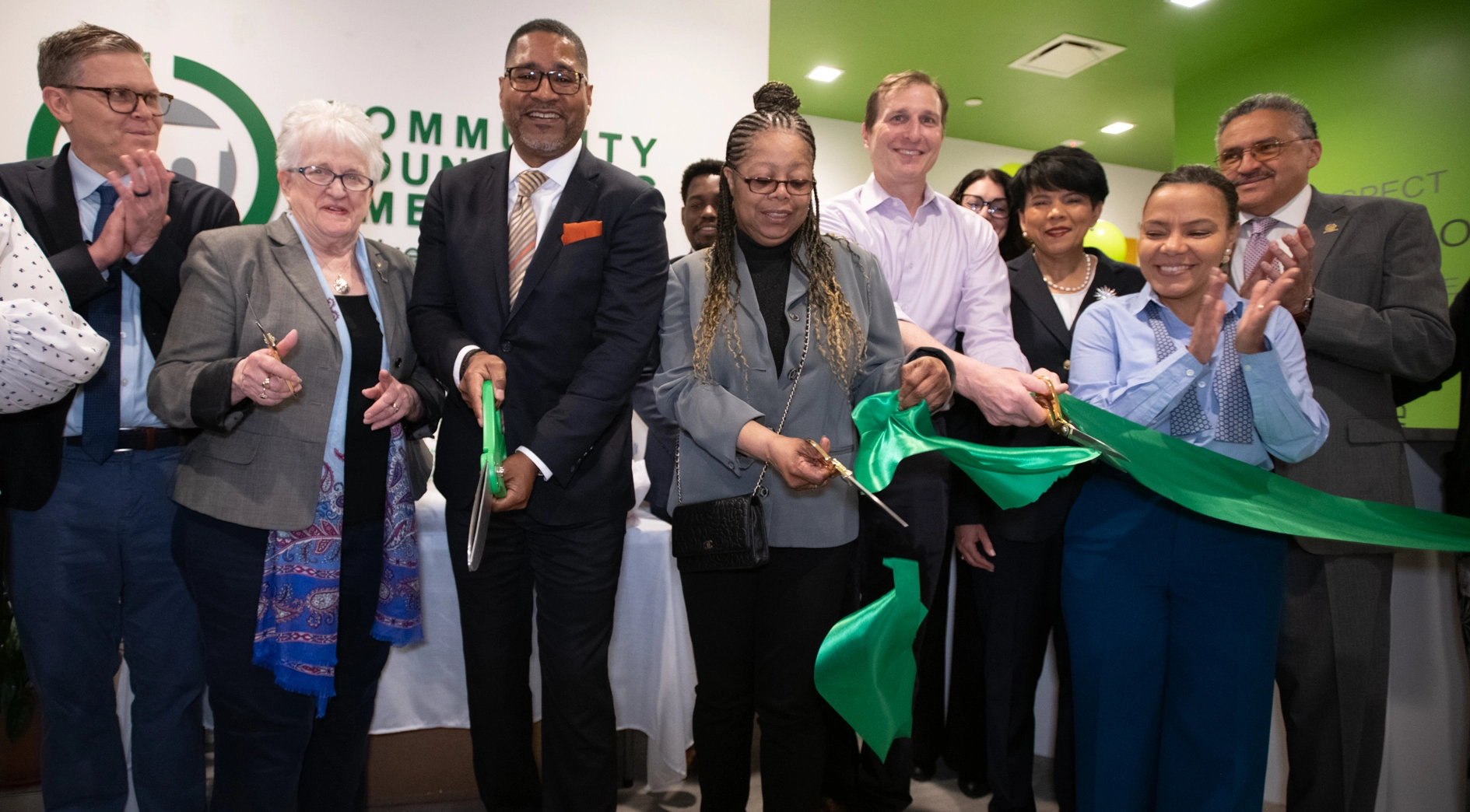 A large group of CCM staff and community and government officials cut a green ribbon to signify the grand opening of the Bond Street Clinic.